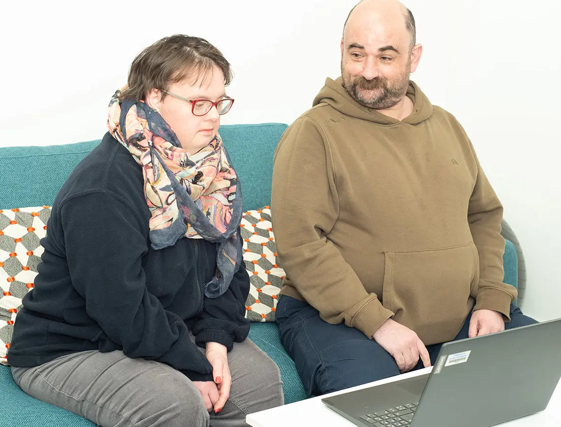 Two people sitting on a sofa looking at a laptop.