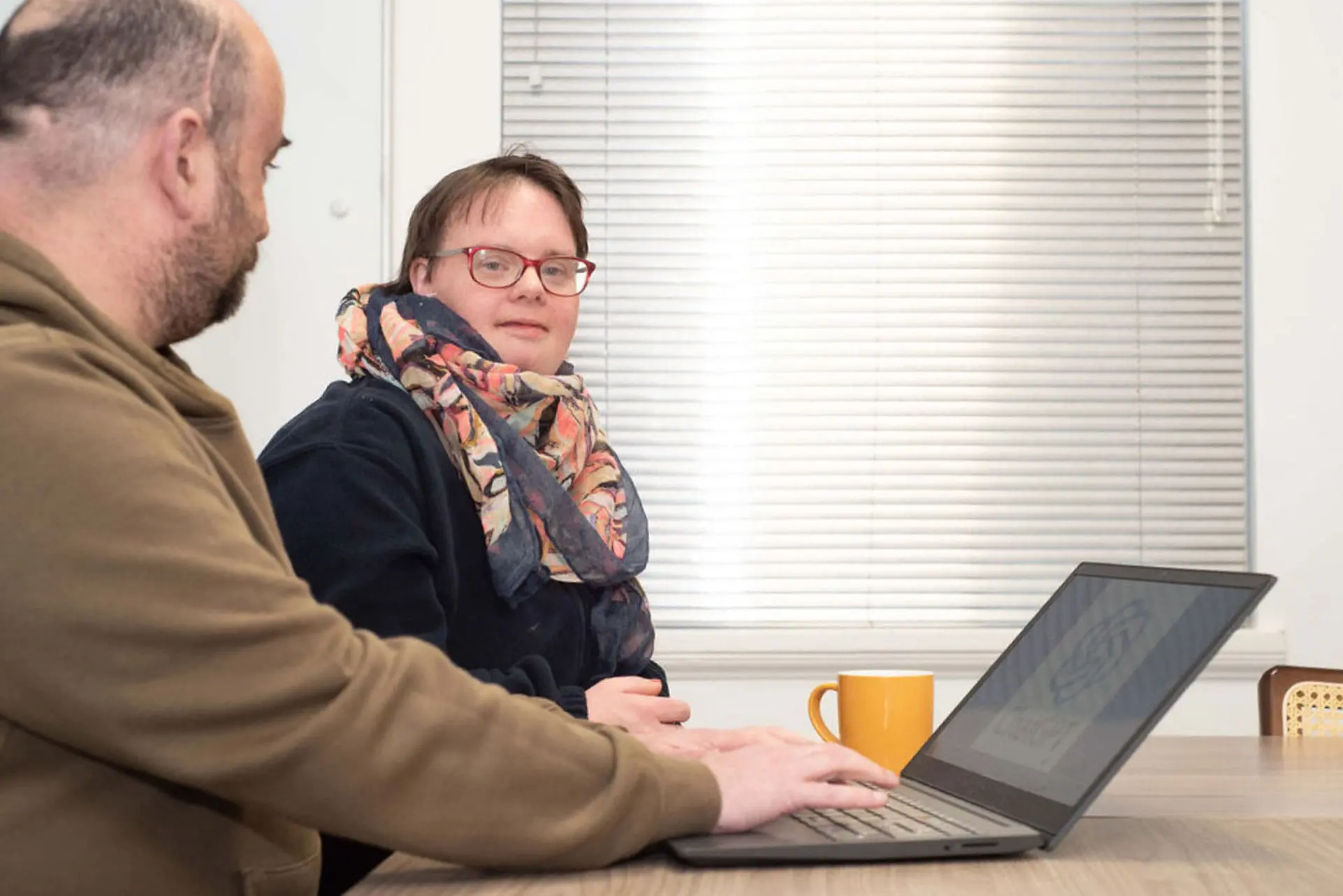 Two people seated at a table, looking at a laptop during a meeting.